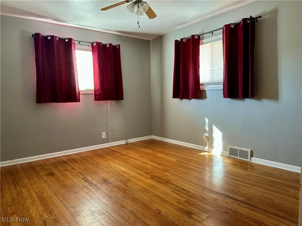 Unfurnished room with healthy amount of natural light, wood-type flooring, a ceiling fan, and a textured ceiling