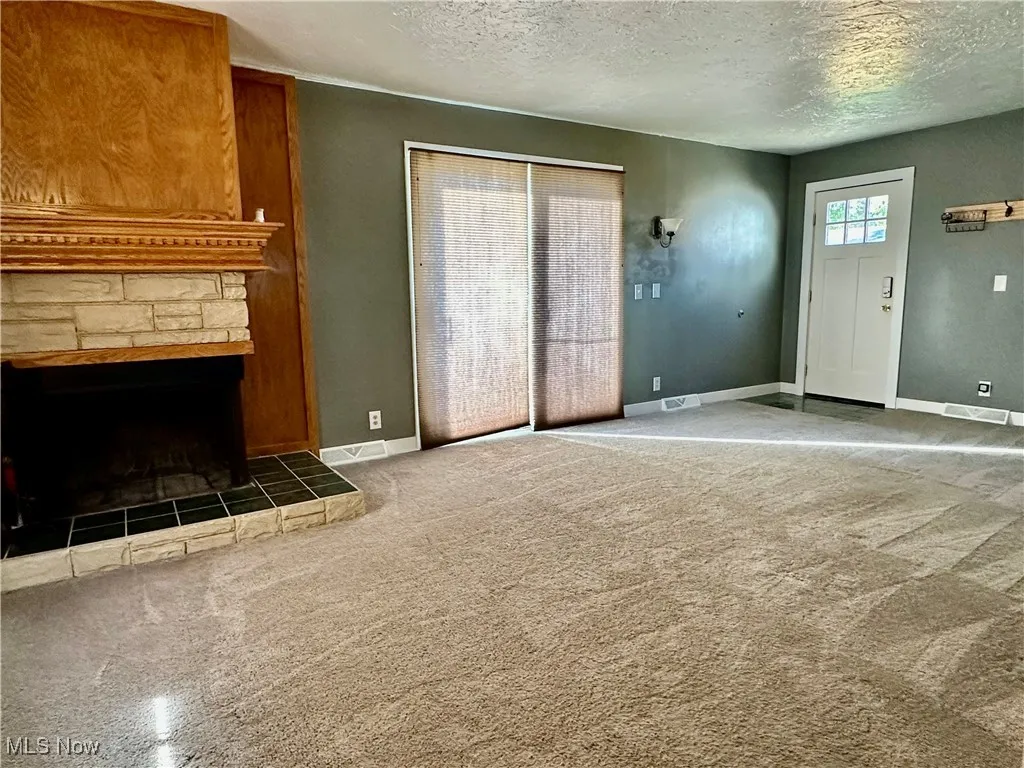 first floor family room with sliding doors to backyard Unfurnished living room with light carpet, a stone fireplace, and a textured ceiling