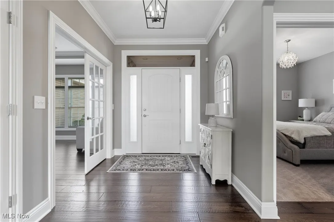 Foyer entrance with a chandelier, dark wood-style flooring, and crown molding