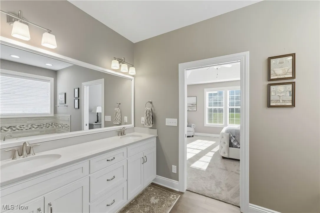 Full bathroom featuring double vanity, ensuite bath, light wood-style floors, and backsplash
