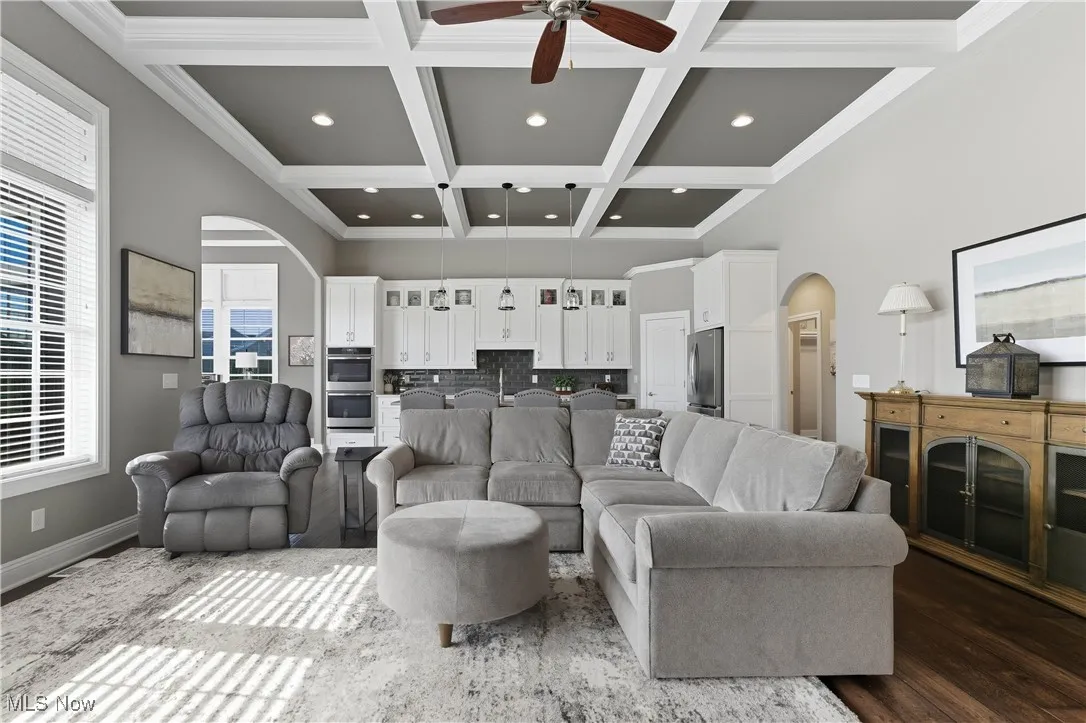 Living room with arched walkways, beam ceiling, coffered ceiling, ceiling fan, and wood finished floors
