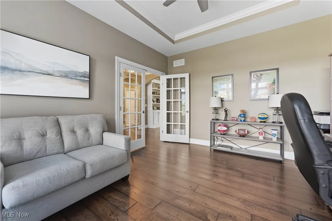 Office space with a tray ceiling, french doors, wood-type flooring, ornamental molding, and ceiling fan