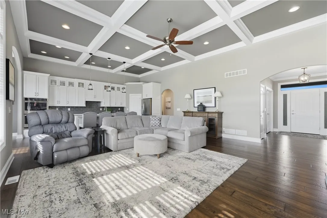 Living room featuring arched walkways, coffered ceiling, beam ceiling, dark wood-style flooring, and recessed lighting