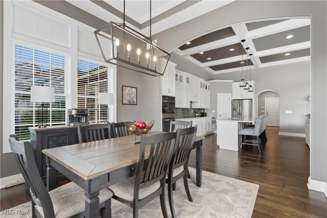Dining space featuring dark wood-type flooring, arched walkways, coffered ceiling, beam ceiling, and recessed lighting