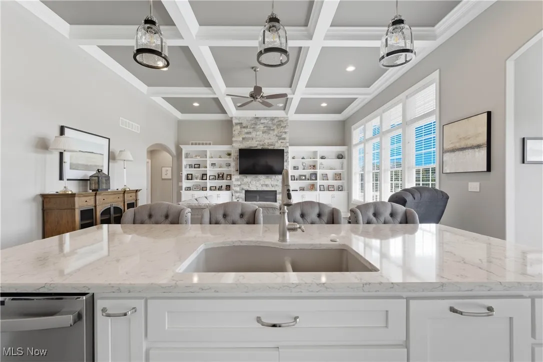 Kitchen with white cabinetry, light stone counters, a fireplace, stainless steel dishwasher, and beamed ceiling