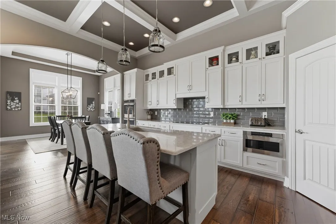 Kitchen with light stone countertops, white cabinets, pendant lighting, tasteful backsplash, and a breakfast bar area