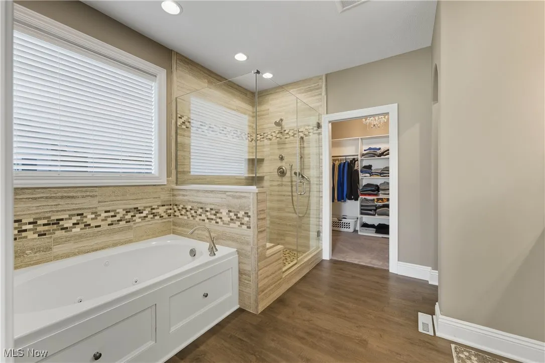 Full bath with a tub with jets, a spacious closet, a stall shower, dark wood-type flooring, and recessed lighting