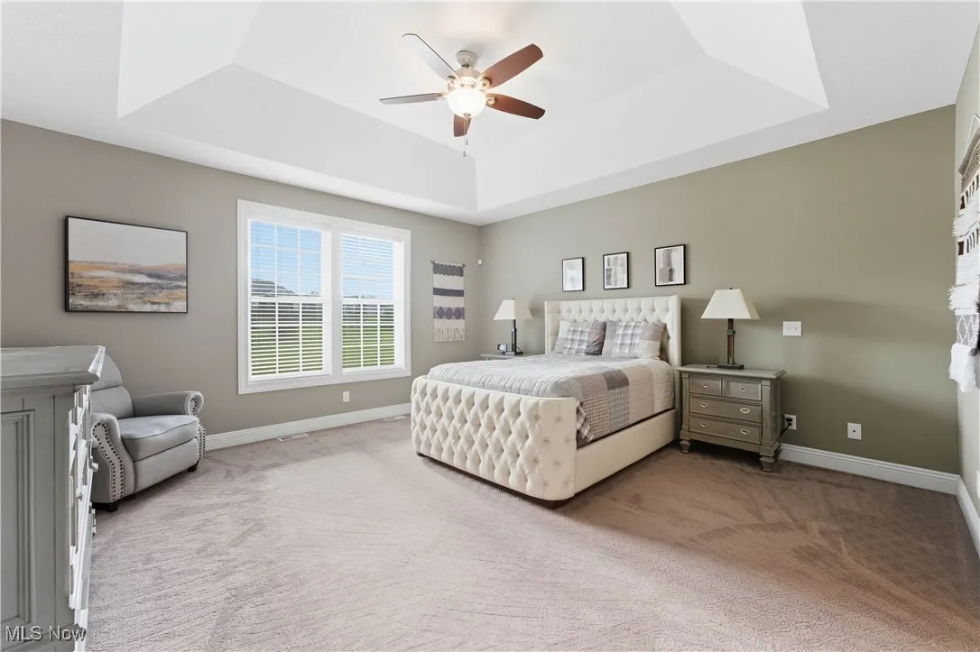 Bedroom with light carpet, a tray ceiling, and ceiling fan