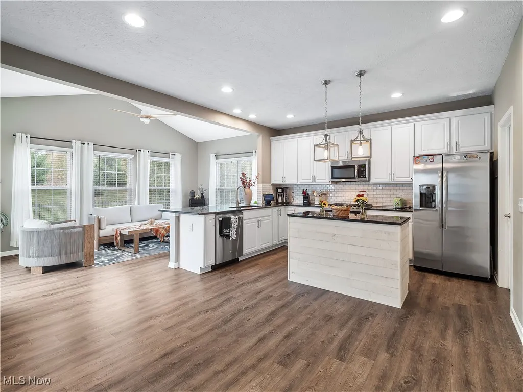 Kitchen featuring appliances with stainless steel finishes, white cabinets, dark wood finished floors, pendant lighting, and backsplash