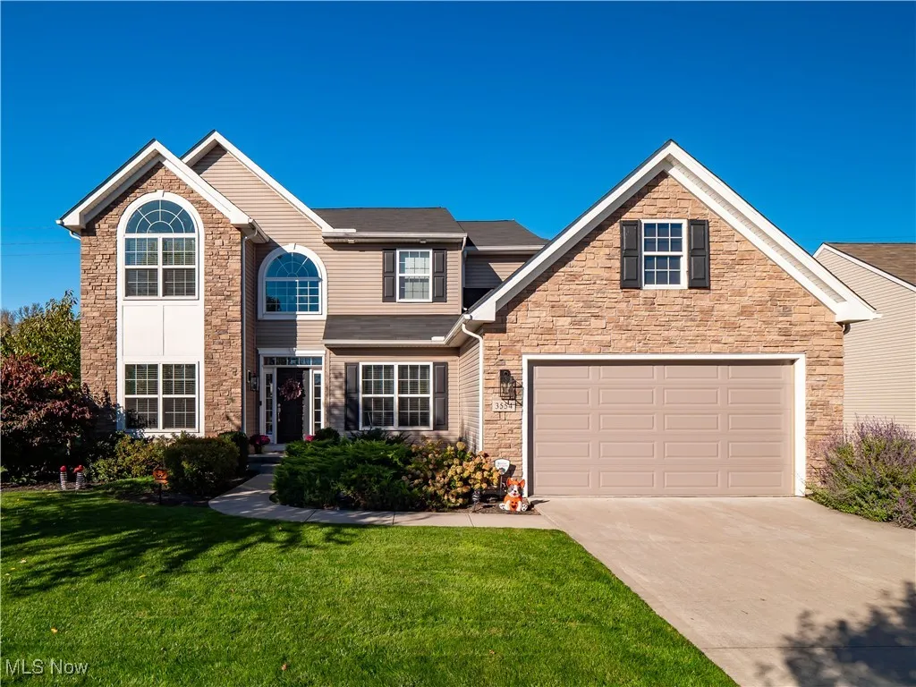 Traditional home featuring a front yard, concrete driveway, a garage, and stone siding