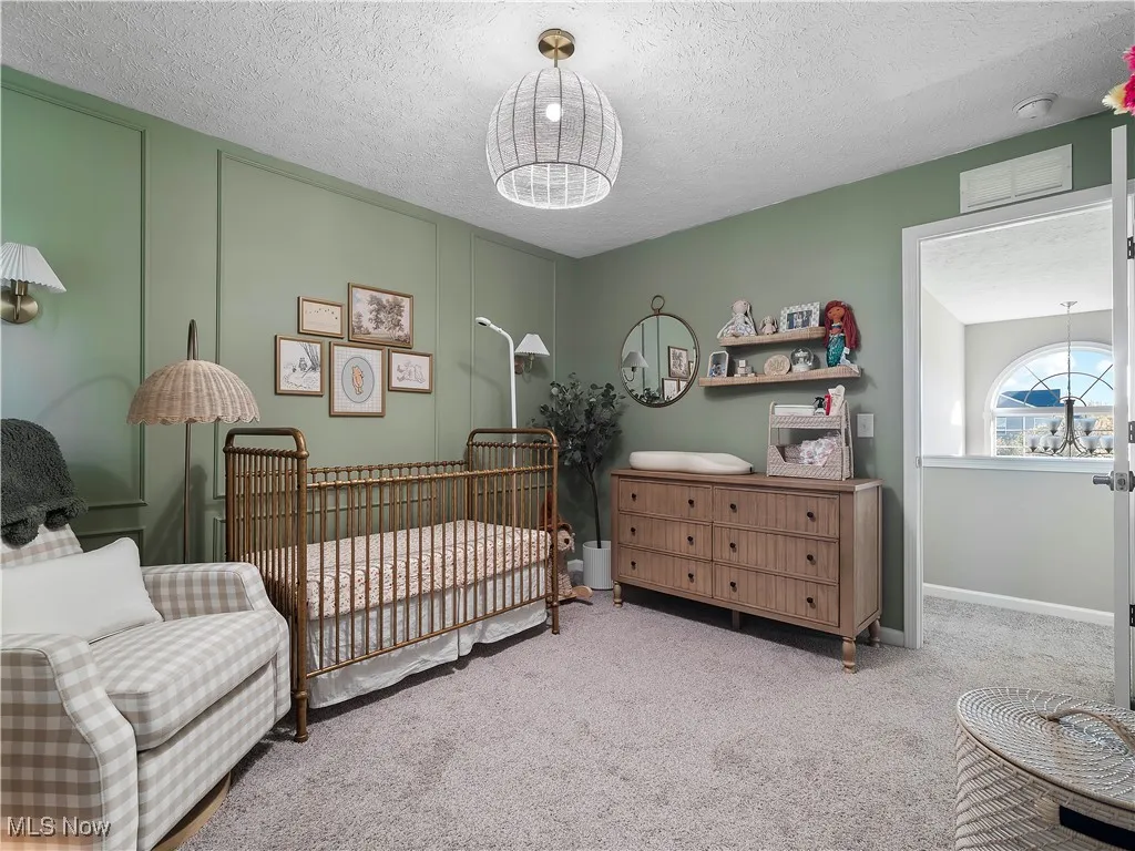 Bedroom with carpet flooring, a crib, a textured ceiling, a chandelier, and a decorative wall