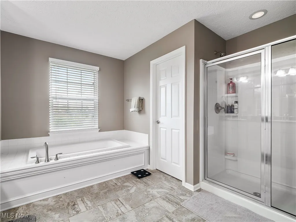 Bathroom with a textured ceiling, a shower stall, and a garden tub