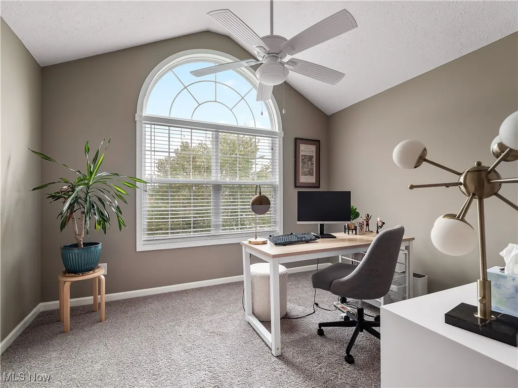 Home office featuring vaulted ceiling, light carpet, a ceiling fan, and a textured ceiling