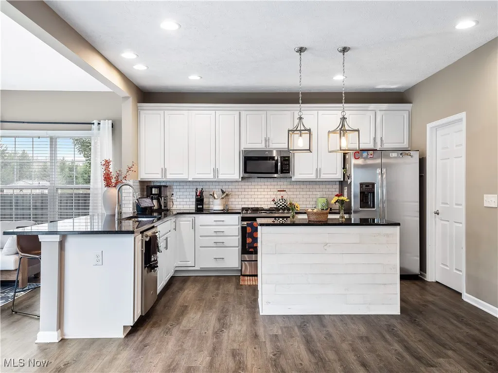 Kitchen featuring dark stone countertops, appliances with stainless steel finishes, white cabinetry, dark wood-style flooring, and decorative light fixtures