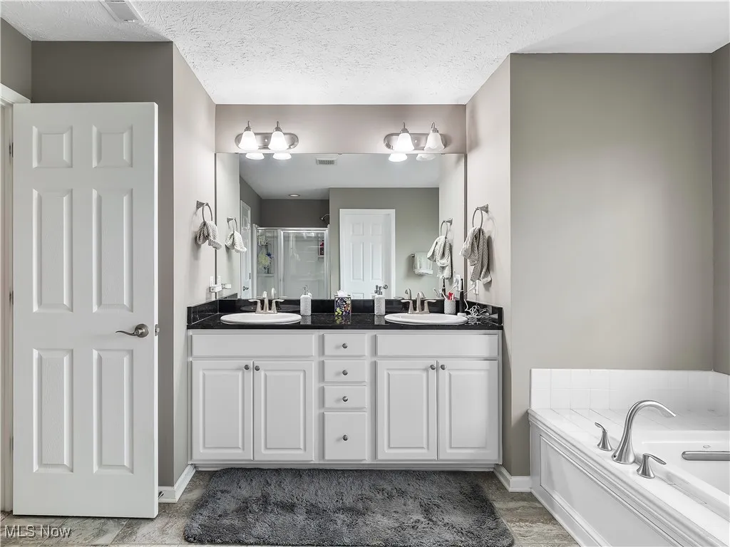 Full bath featuring a stall shower, double vanity, a bath, and a textured ceiling