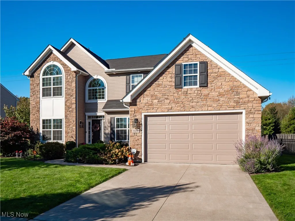 Traditional-style home featuring stone siding, a front lawn, and concrete driveway