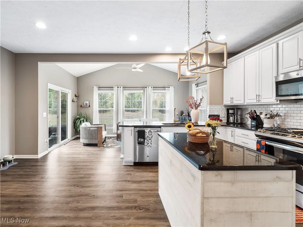 Kitchen with dark stone counters, white cabinets, appliances with stainless steel finishes, vaulted ceiling, and pendant lighting