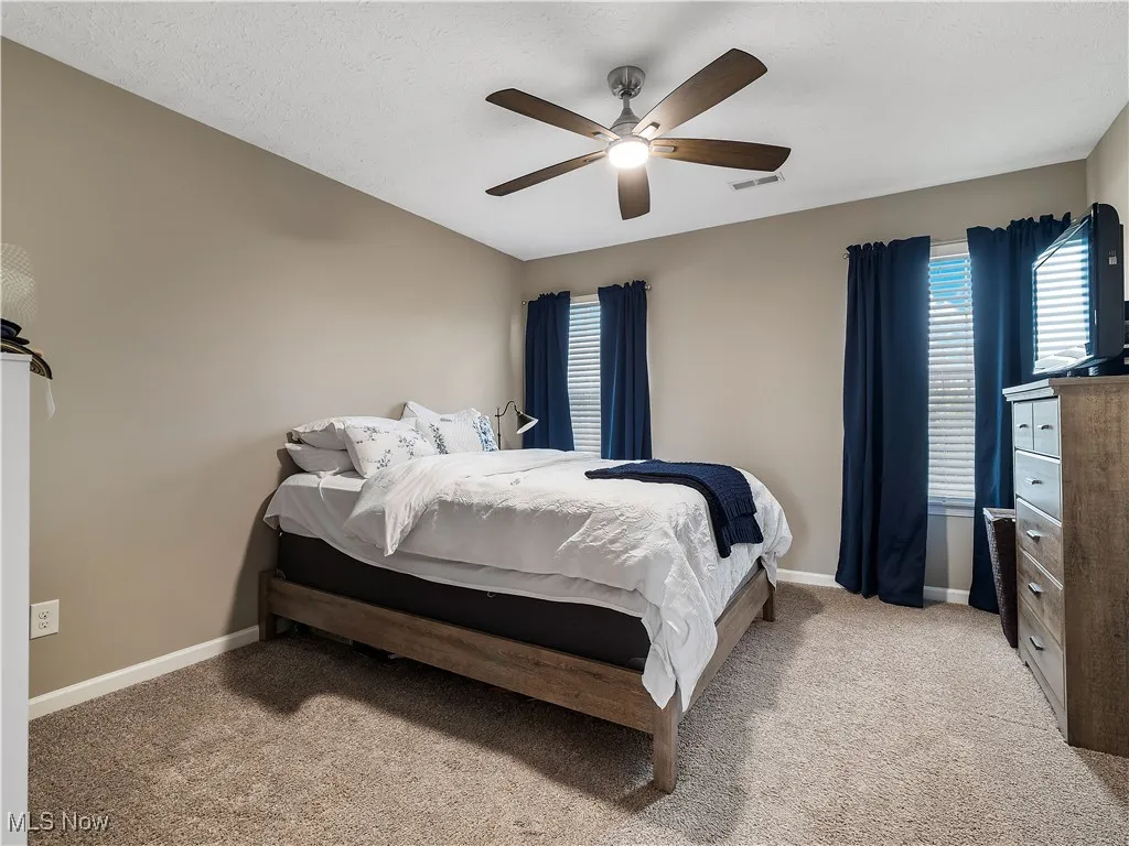 Bedroom with light carpet, ceiling fan, and a textured ceiling