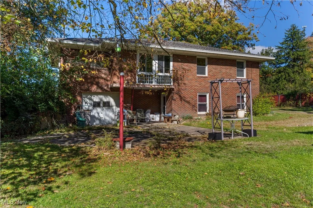 Back of property with a balcony, brick siding, a lawn, a patio, and an attached garage