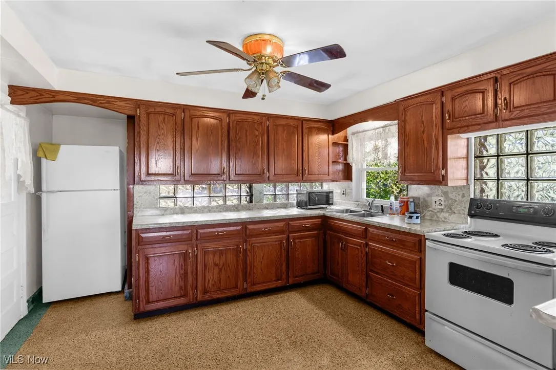 Kitchen with white appliances, open shelves, light countertops, brown cabinets, and ceiling fan