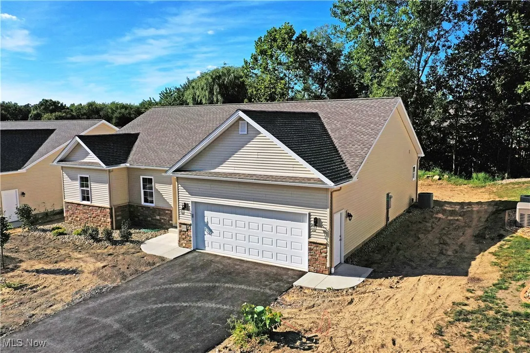 View of front of house with stone siding, driveway, and a shingled roof