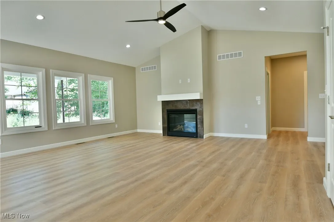 Unfurnished living room featuring recessed lighting, a tiled fireplace, a ceiling fan, light wood-style floors, and high vaulted ceiling