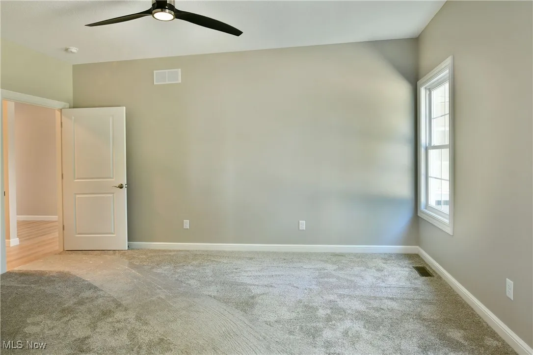 Unfurnished bedroom with light colored carpet and ceiling fan