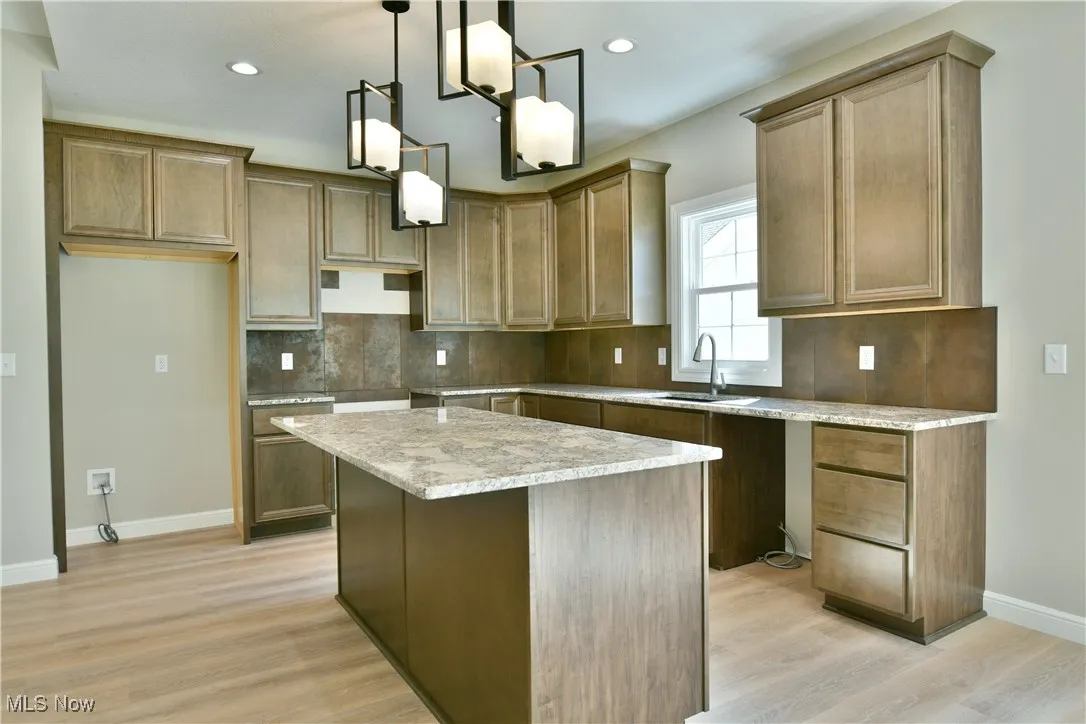 Kitchen with tasteful backsplash, pendant lighting, recessed lighting, a center island, and light wood-style floors