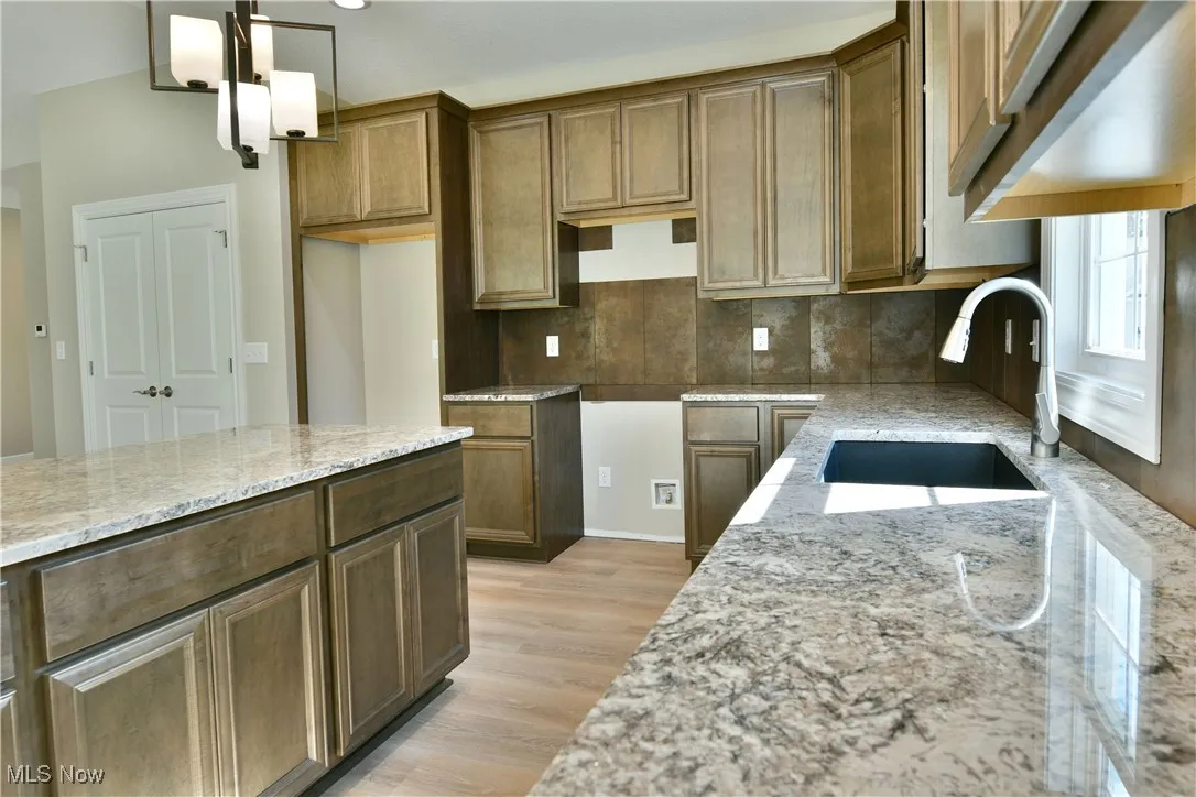 Kitchen featuring light stone countertops, brown cabinetry, light wood finished floors, and decorative backsplash