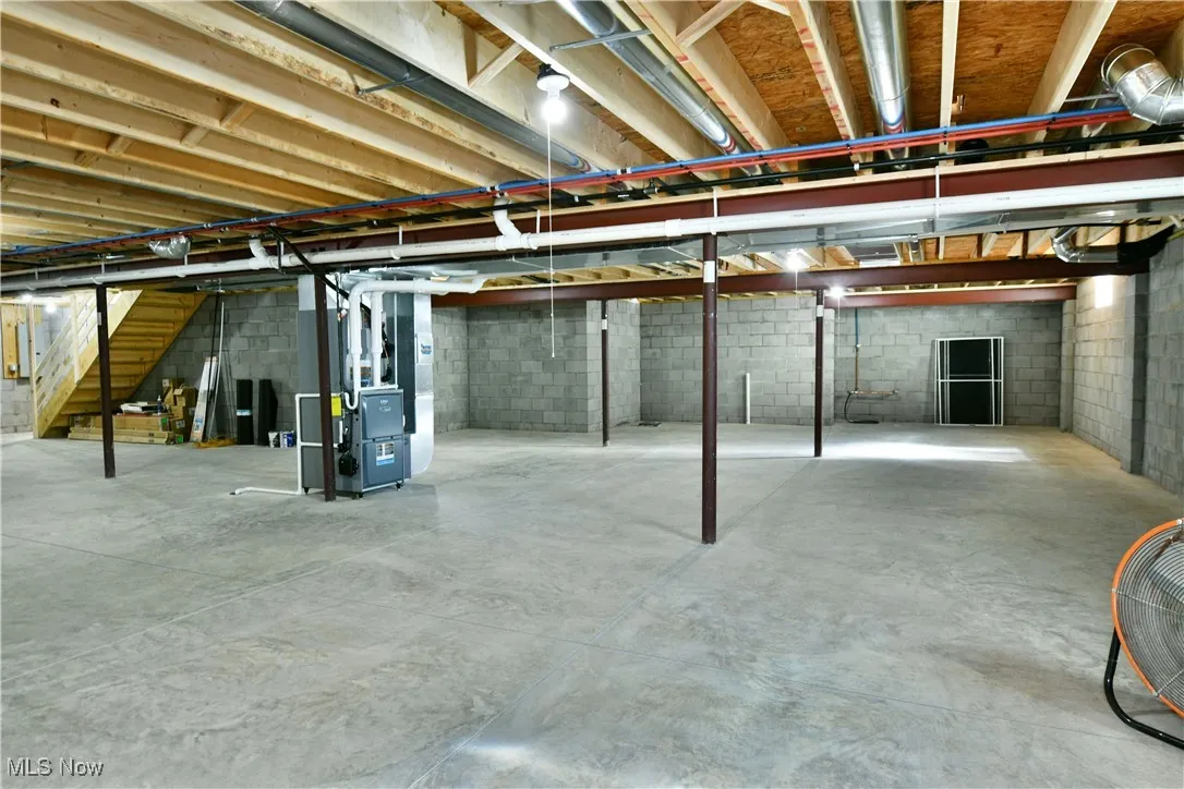Unfinished basement featuring stairs and heating unit