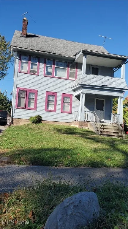 View of front of home with a front yard, a chimney, and covered porch