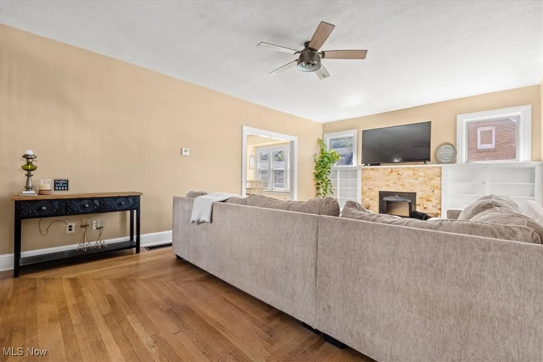 Living room featuring a fireplace, wood finished floors, a textured ceiling, and ceiling fan