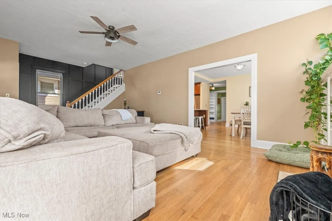 Living room featuring wood-type flooring, ceiling fan, and stairway