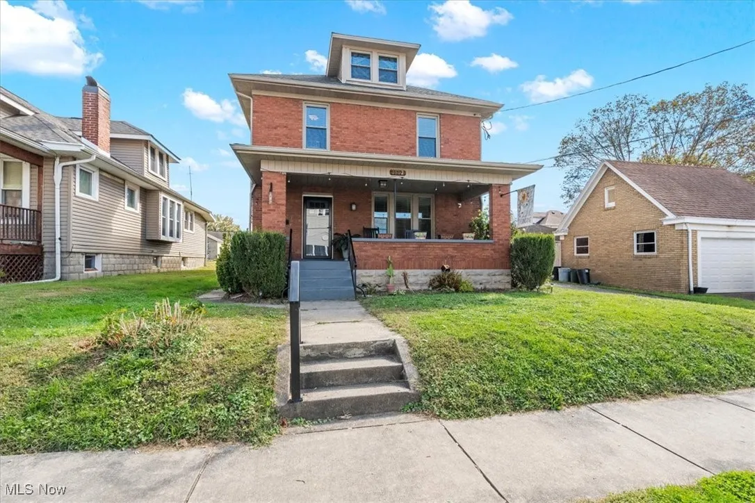 American foursquare style home featuring a porch, brick siding, and a front lawn