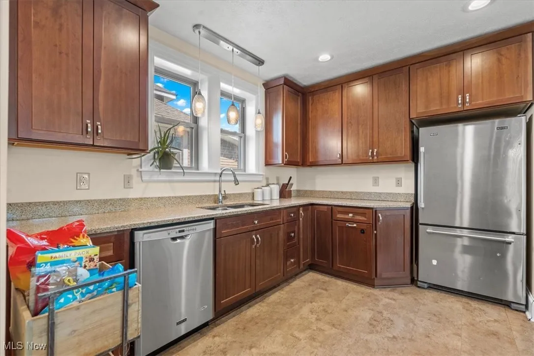 Kitchen with stainless steel appliances, light stone counters, decorative light fixtures, and brown cabinetry