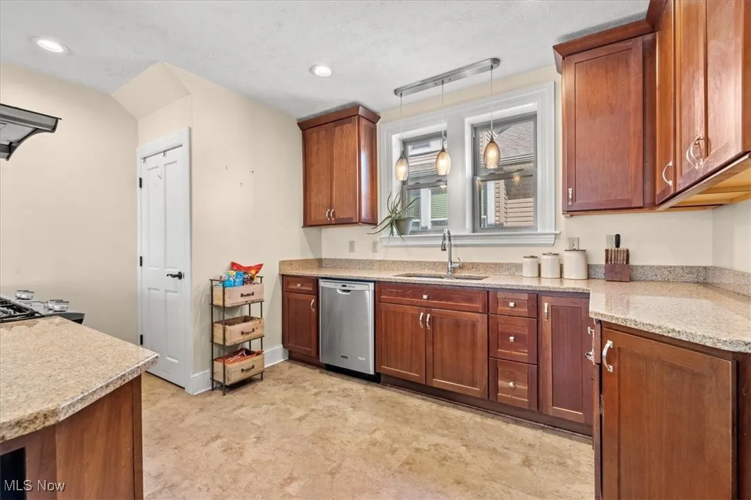 Kitchen featuring decorative light fixtures, light stone counters, dishwasher, brown cabinets, and a textured ceiling