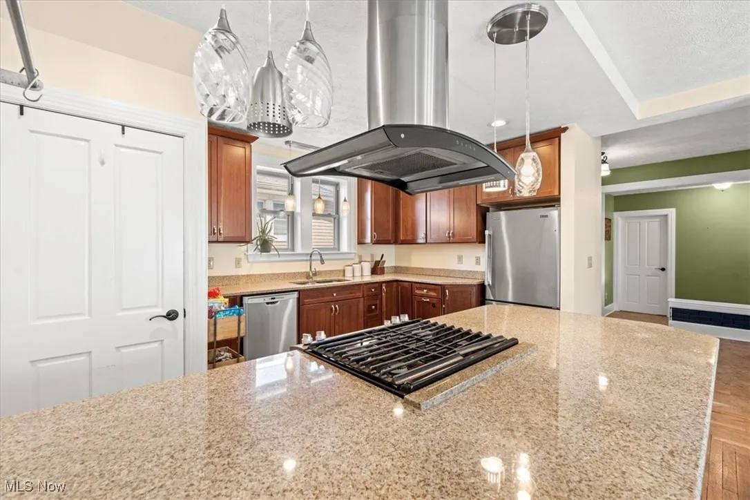 Kitchen with island range hood, appliances with stainless steel finishes, light stone counters, decorative light fixtures, and recessed lighting