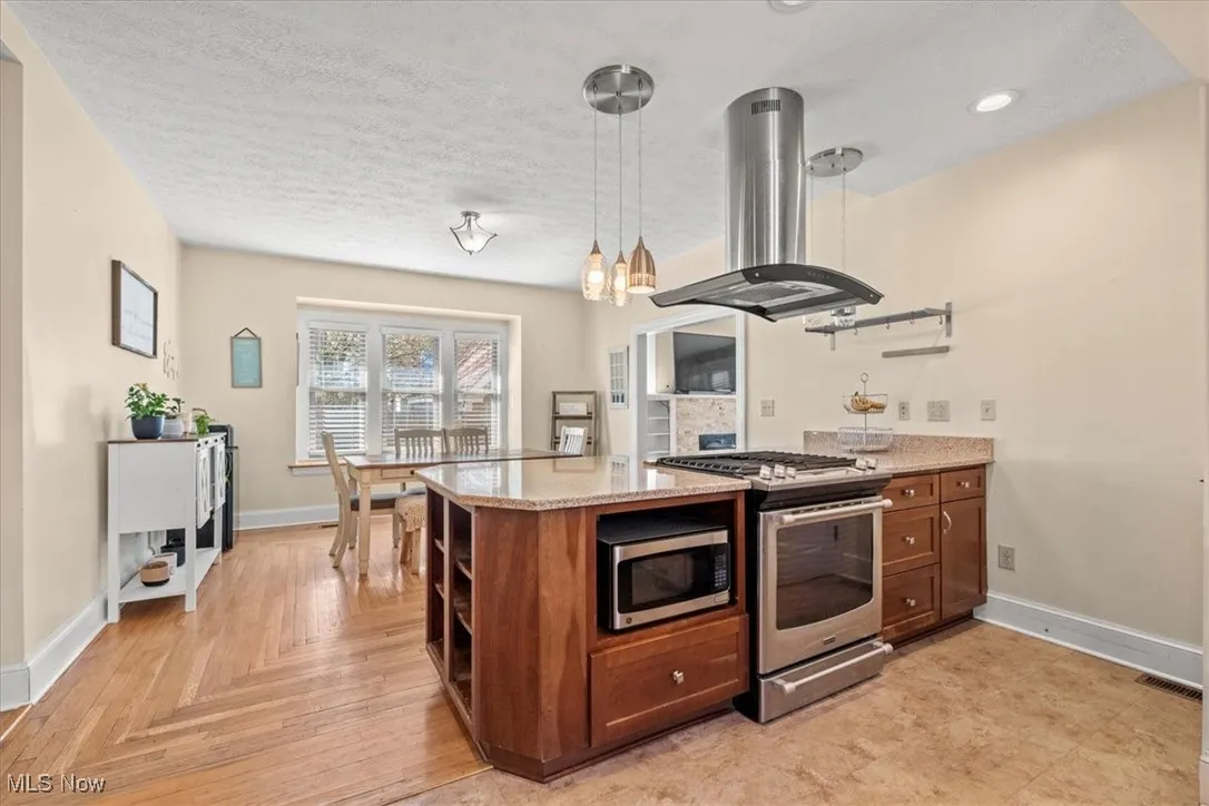 Kitchen featuring open shelves, island range hood, stainless steel appliances, light stone counters, and a textured ceiling