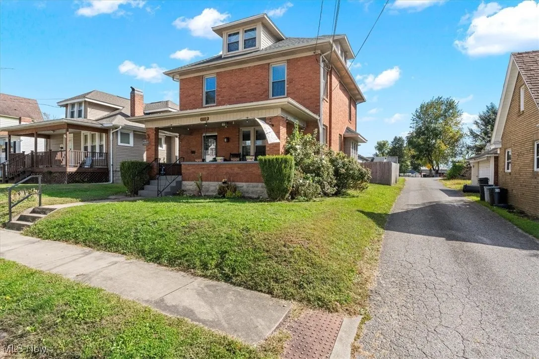 American foursquare style home featuring brick siding, a porch, and a front lawn