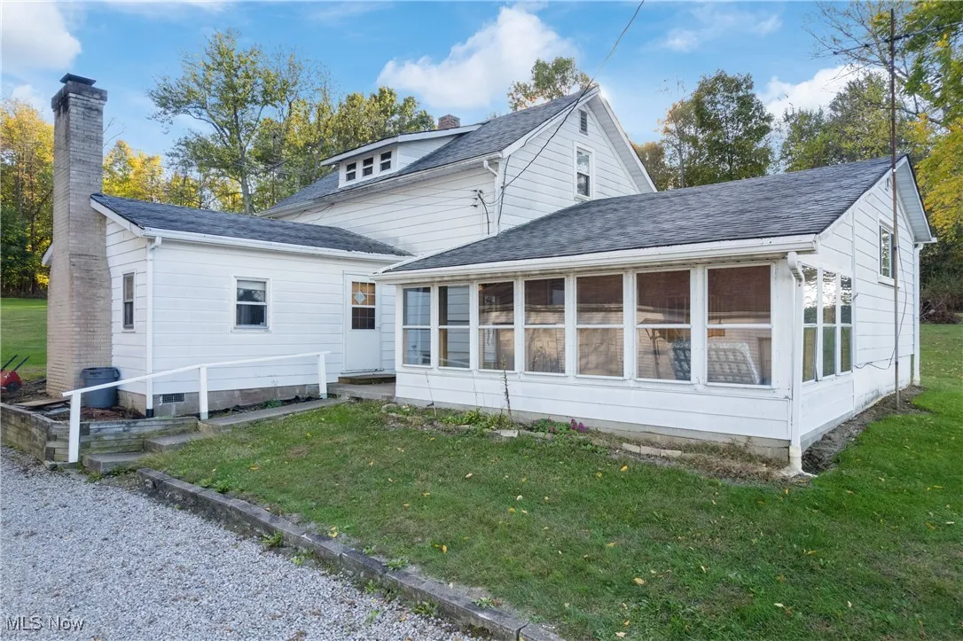 Rear view of property featuring a sunroom, a chimney, a lawn, and roof with shingles
