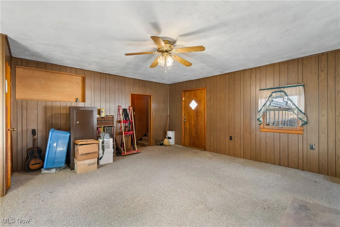 Unfurnished living room with carpet floors, a ceiling fan, wood walls, stairs, and a textured ceiling