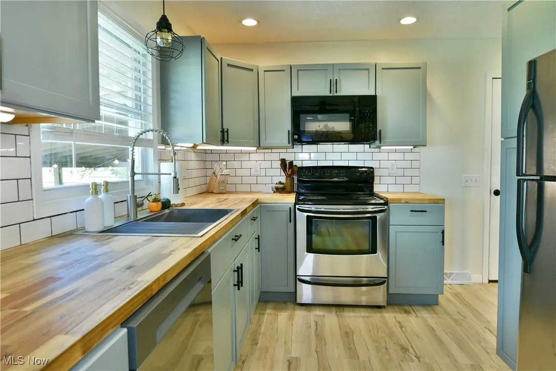 Kitchen featuring appliances with stainless steel finishes, tasteful backsplash, wood counters, pendant lighting, and recessed lighting