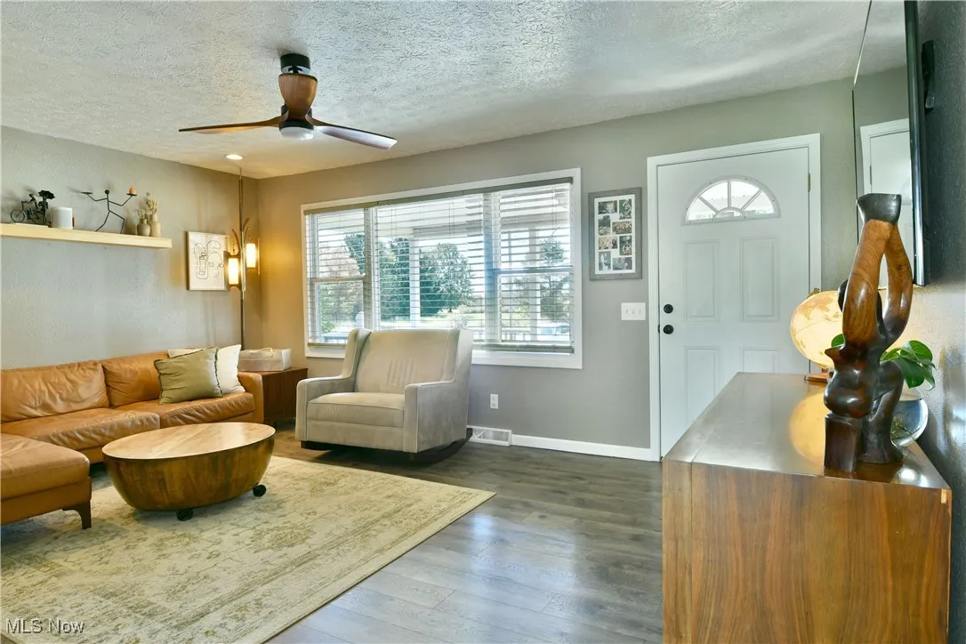 Living area with dark wood-type flooring, a textured ceiling, and a ceiling fan