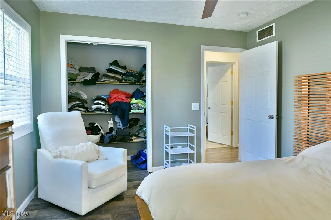 Bedroom with a textured ceiling, multiple windows, wood finished floors, and ceiling fan