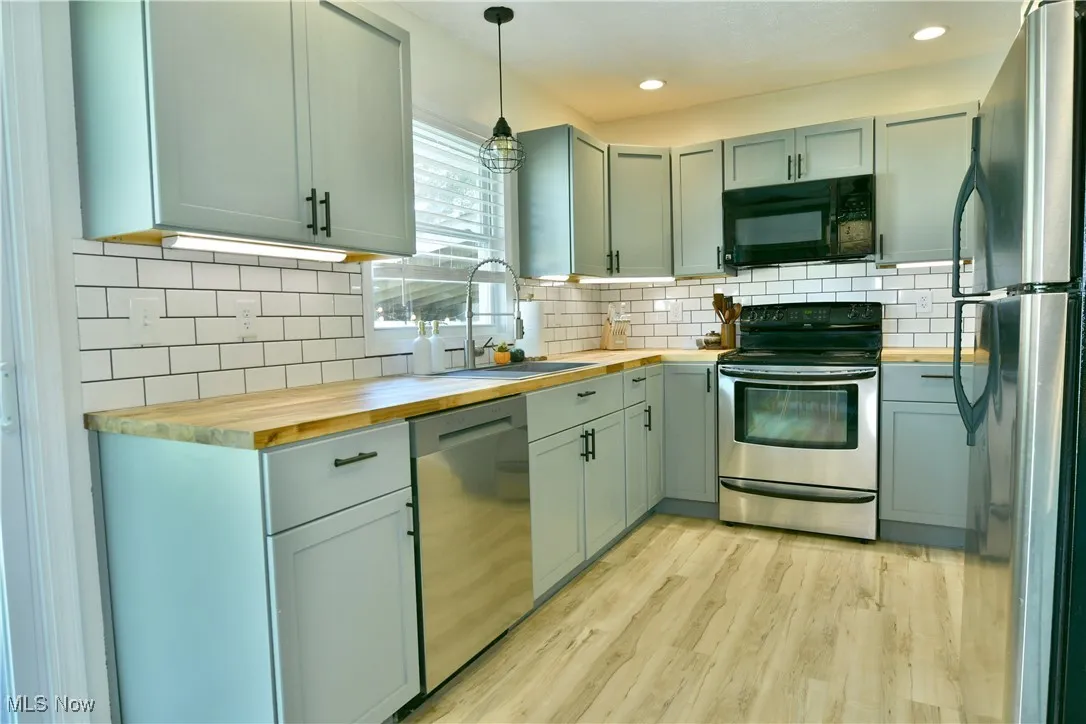 Kitchen featuring pendant lighting, stainless steel appliances, wooden counters, light wood-style flooring, and backsplash