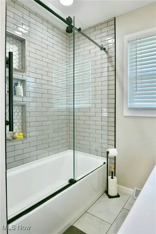 Full bath with combined bath / shower with glass door and tile patterned floors