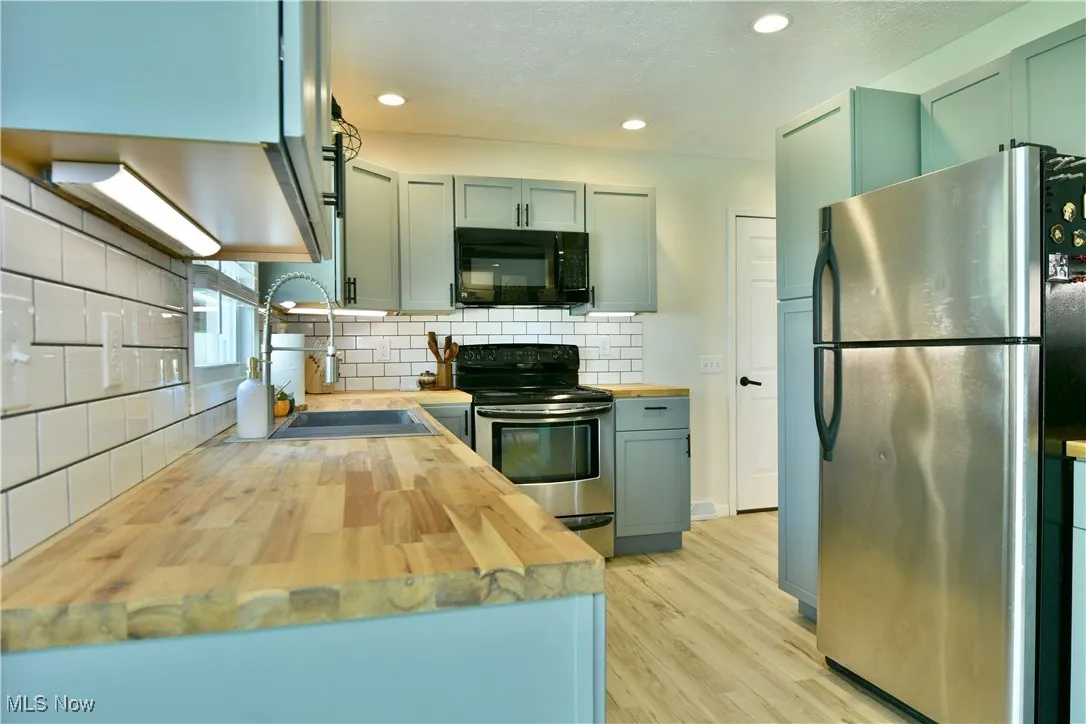 Kitchen with butcher block countertops, appliances with stainless steel finishes, light wood finished floors, backsplash, and recessed lighting