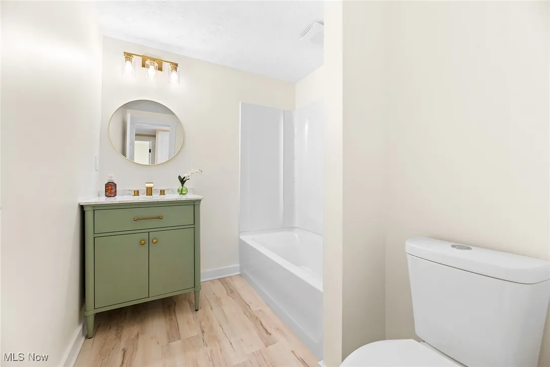 Bathroom with vanity, light wood finished floors, bathtub / shower combination, and a textured ceiling