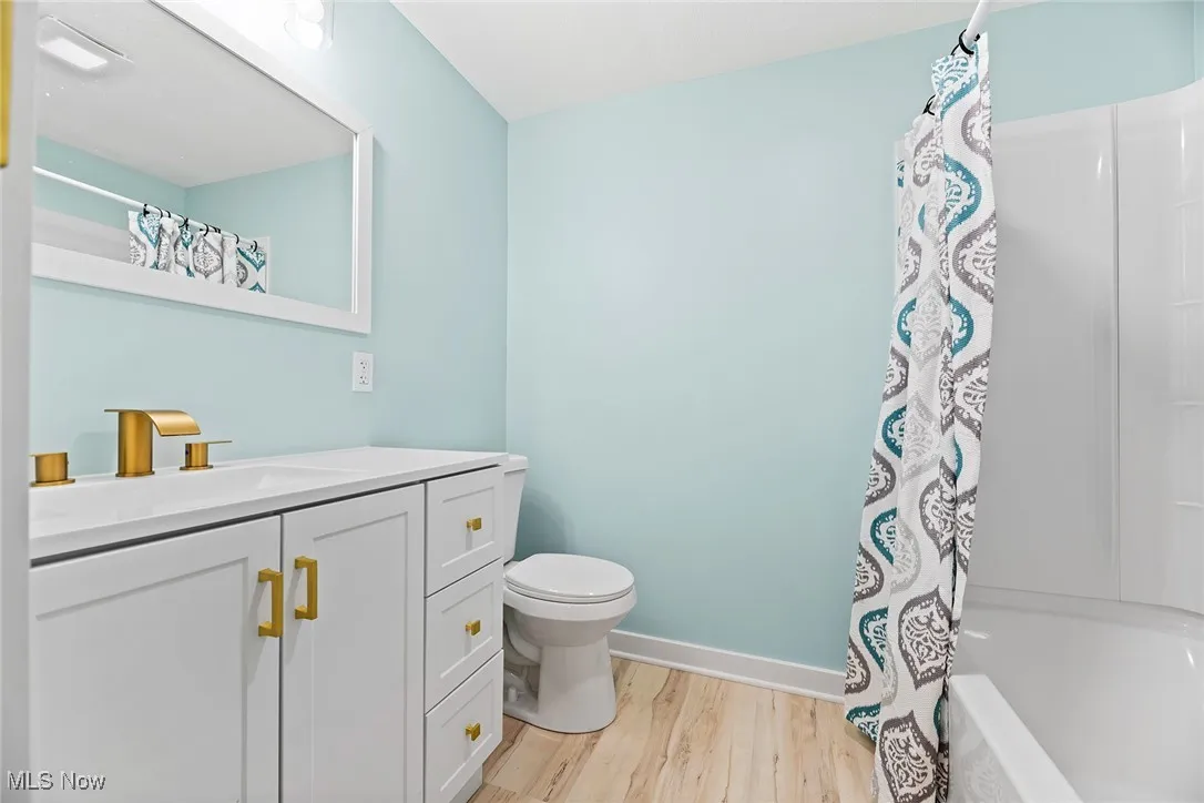 Full bath with light wood-type flooring, vanity, and shower / bath combo with shower curtain