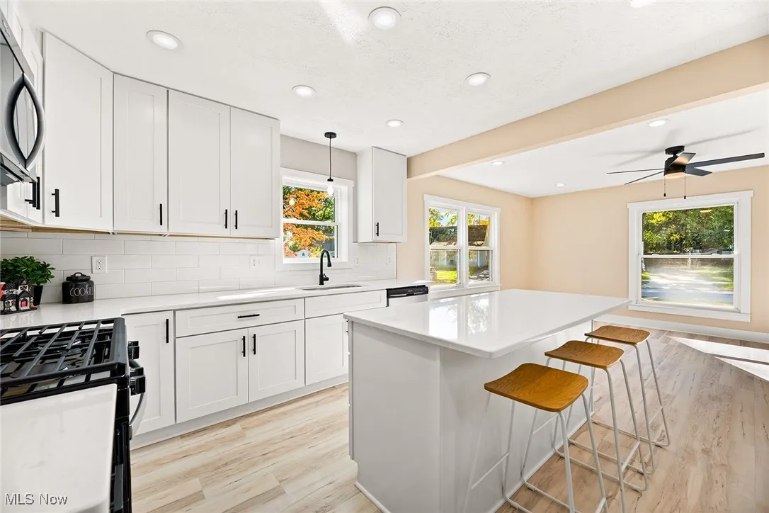 Kitchen with white cabinets, a breakfast bar area, light wood-type flooring, decorative light fixtures, and healthy amount of natural light